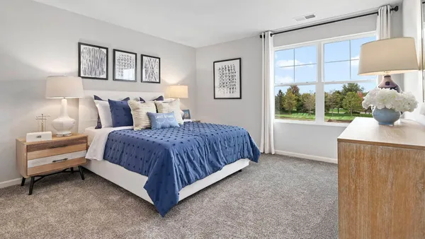 a spacious bedroom with a bed and a lamp on dresser