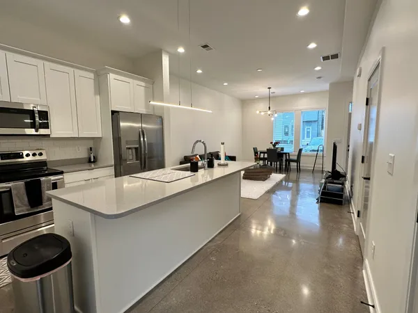 a kitchen with stainless steel appliances a sink a stove a refrigerator cabinets and chairs