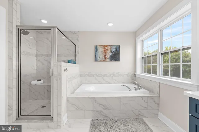 a bathroom with a tub a window and glass door shower