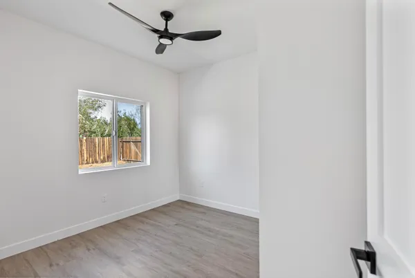 an empty room with wooden floor ceiling fan and windows