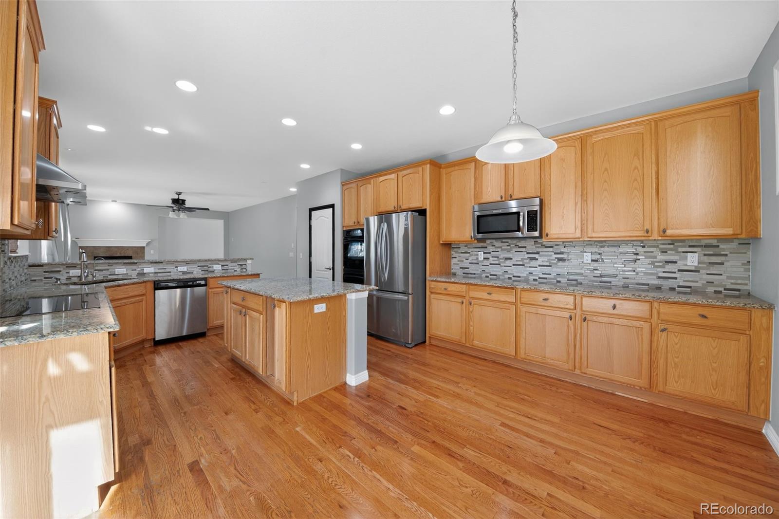 11036 Glengate Circle Highlands Ranch, CO 80130 - Photo 18 of 31 a kitchen with stainless steel appliances kitchen island granite countertop a stove a sink a refrigerator and white cabinets with wooden floor