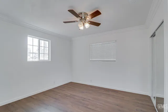 a view of an empty room with wooden floor and ceiling fan