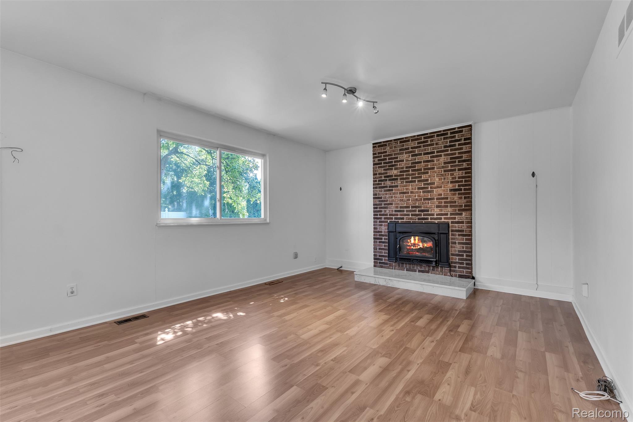 7000 Woonsocket Street Canton, MI 48187 - Photo 29 of 65 Interior space featuring wood-finish flooring, a brick fireplace with a stone hearth, a track lighting fixture, a large window, and white walls