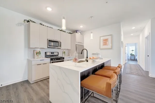 a kitchen with stainless steel appliances granite countertop a sink a stove a refrigerator cabinets and a dining table with wooden floor