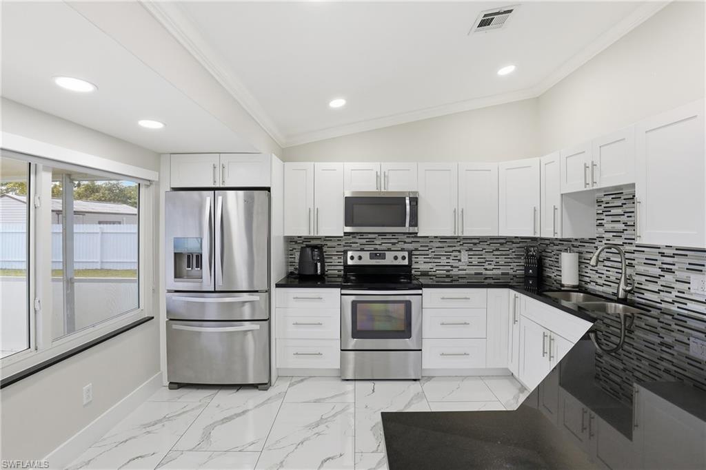 5312 17th Avenue Southwest Naples, FL 34116 - Photo 11 of 45 Kitchen with vaulted ceiling, stainless steel appliances, decorative backsplash, white cabinetry, and dark stone countertops