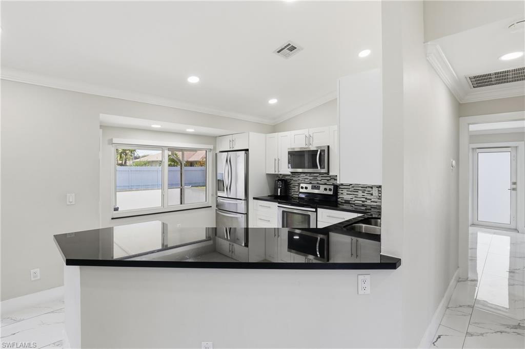 5312 17th Avenue Southwest Naples, FL 34116 - Photo 12 of 45 Kitchen with light marble finish floors, ornamental molding, stainless steel appliances, white cabinetry, and vaulted ceiling