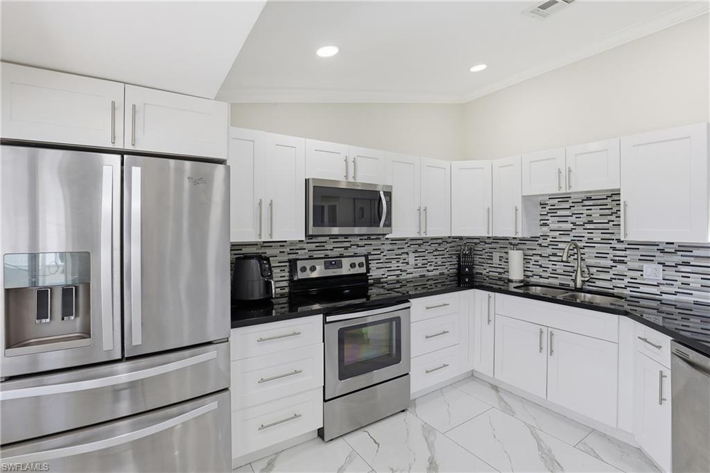 5312 17th Avenue Southwest Naples, FL 34116 - Photo 13 of 45 Kitchen with stainless steel appliances, white cabinets, vaulted ceiling, light marble finish floors, and dark stone countertops
