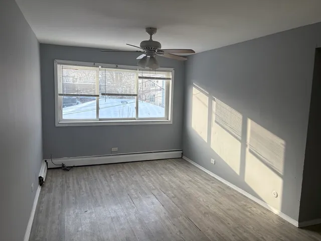 an empty room with wooden floor fan and windows