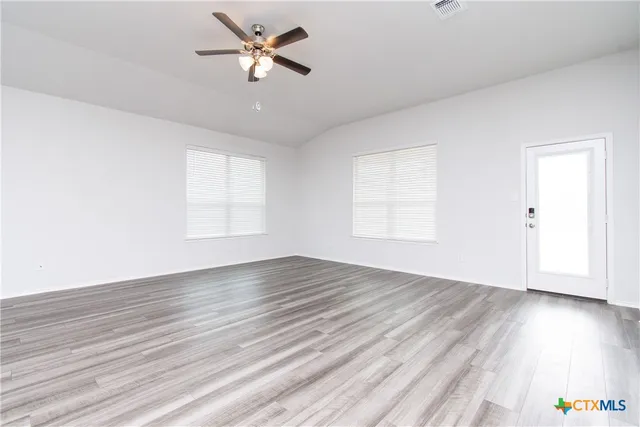an empty room with wooden floor ceiling fan and windows