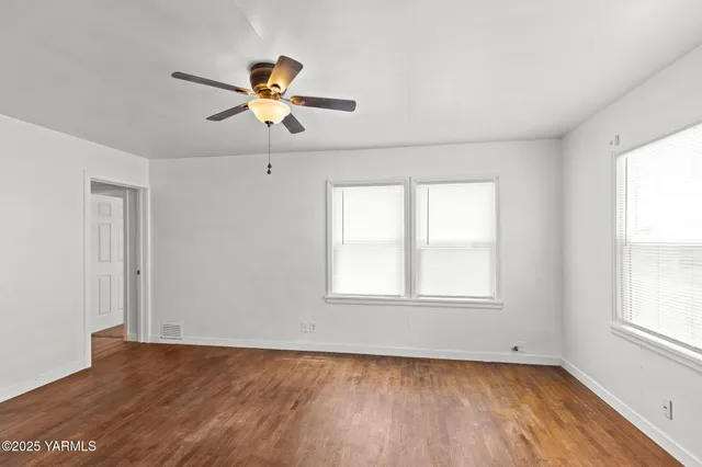 a view of empty room with wooden floor and fan