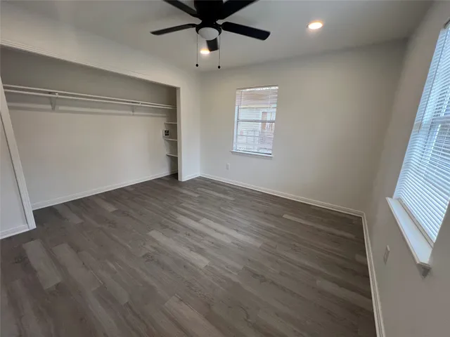 an empty room with wooden floor fan and windows