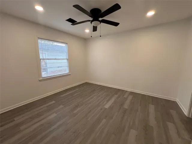 an empty room with wooden floor ceiling fan and windows