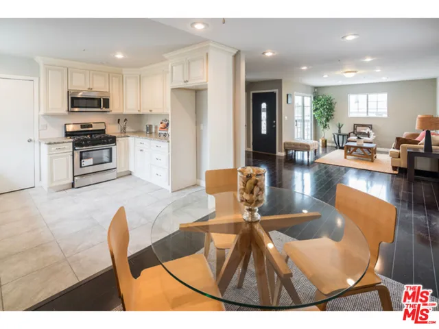 a kitchen with stainless steel appliances kitchen island granite countertop a refrigerator a stove a sink a dining table and chairs with wooden floor