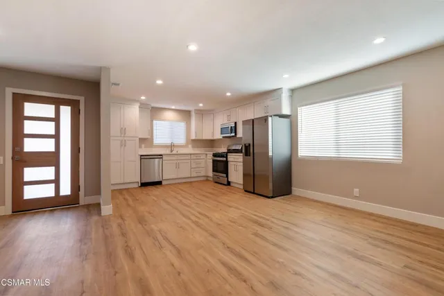 a view of kitchen with stainless steel appliances granite countertop a stove top oven a refrigerator with white cabinets and wooden floor