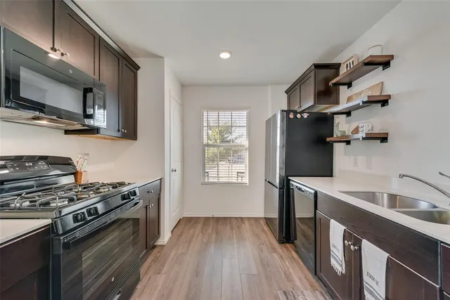 a kitchen with stainless steel appliances a sink dishwasher stove and microwave with wooden floor
