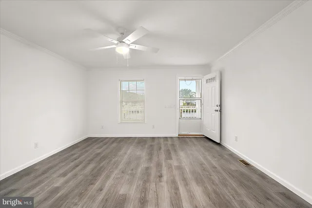 an empty room with wooden floor fan and windows