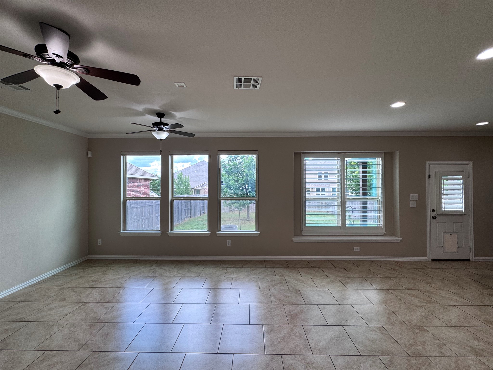 2605 Rough Berry Road Pflugerville, TX 78660 - Photo 8 of 40 A well-lit great room features ample windows, a back door, and dual ceiling fans, all set atop durable tile flooring.