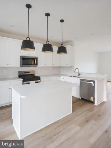 a kitchen with stainless steel appliances granite countertop a stove top oven a sink a refrigerator and white cabinets with wooden floor