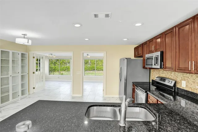 a kitchen with stainless steel appliances granite countertop a refrigerator a stove a sink a dining table and chairs with wooden floor