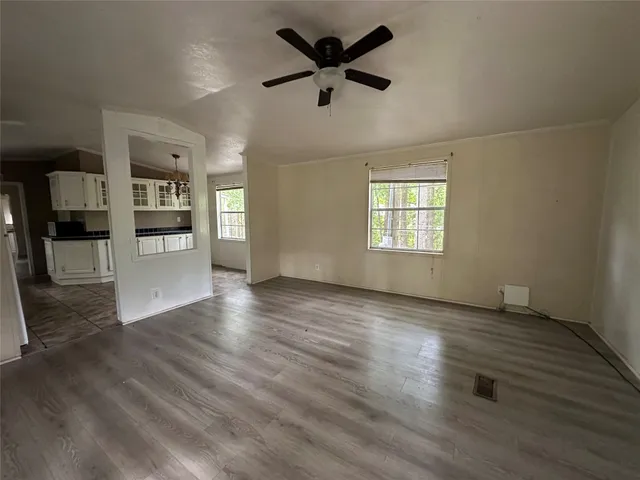 an empty room with wooden floor a ceiling fan and windows