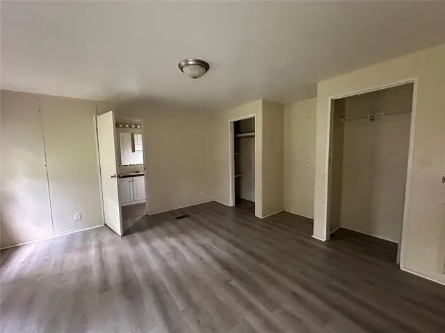an empty room with wooden floor kitchen view and windows