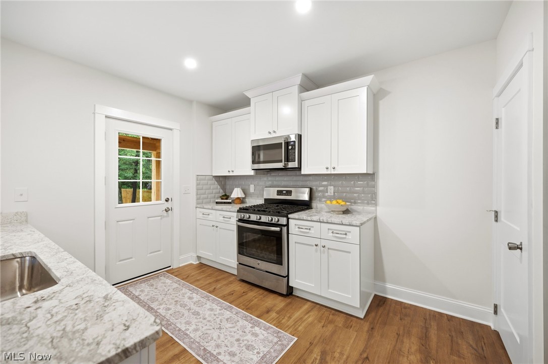 272 Miles Road Chagrin Falls, OH 44022 - Photo 11 of 36 Kitchen featuring white shaker cabinetry, stainless steel appliances, wood Style flooring, light-toned countertops, and a subway tile backsplash