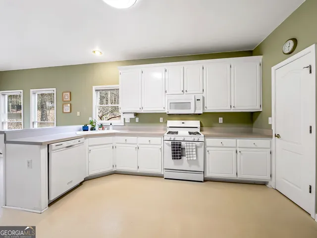 a large white kitchen with granite countertop a sink white cabinets and white appliances