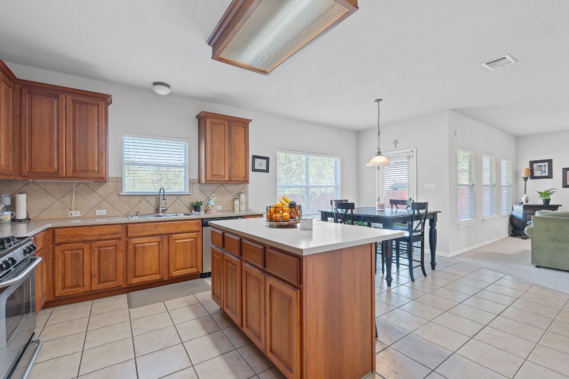 1024 Portchester Castle Path Pflugerville, TX 78660 - Photo 12 of 40 Kitchen with light tile patterned floors, light countertops, brown cabinets, hanging light fixtures, and tasteful backsplash