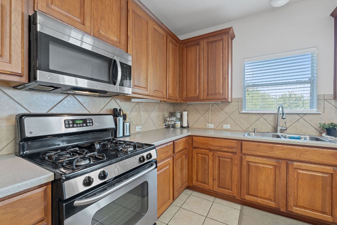 1024 Portchester Castle Path Pflugerville, TX 78660 - Photo 13 of 40 Kitchen featuring stainless steel appliances, light countertops, brown cabinetry, and light tile patterned floors