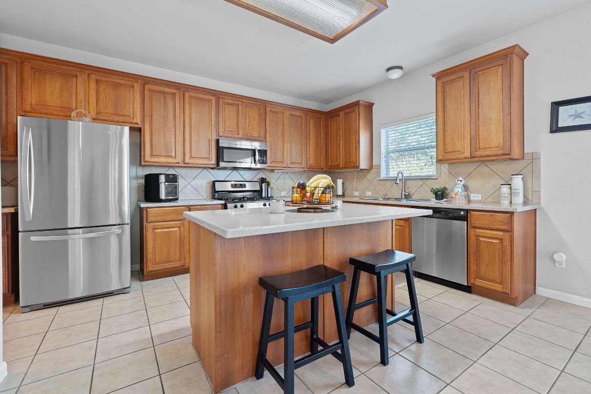 1024 Portchester Castle Path Pflugerville, TX 78660 - Photo 9 of 40 Kitchen with stainless steel appliances, a breakfast bar, brown cabinetry, and light tile patterned floors