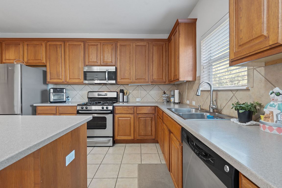 1024 Portchester Castle Path Pflugerville, TX 78660 - Photo 10 of 40 Kitchen with brown cabinets, light tile patterned floors, backsplash, appliances with stainless steel finishes, and light stone countertops