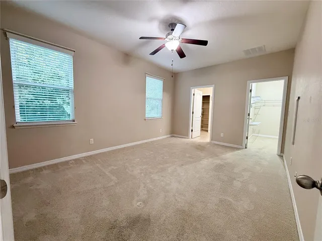 an empty room with chandelier fan and windows