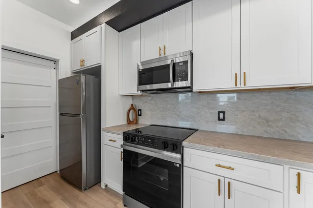 a kitchen with stainless steel appliances white cabinets and a stove a refrigerator with wooden floor