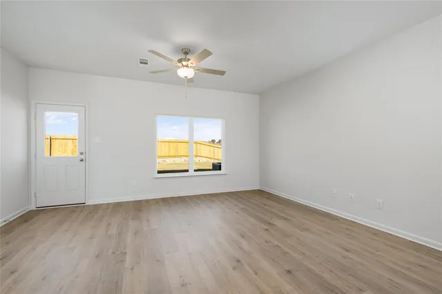 a view of an empty room with wooden floor and a ceiling fan