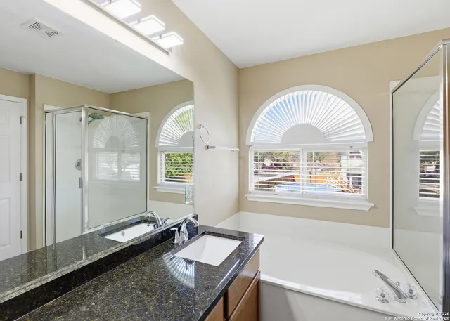 a en suite bathroom with a granite countertop tub a sink and a large mirror
