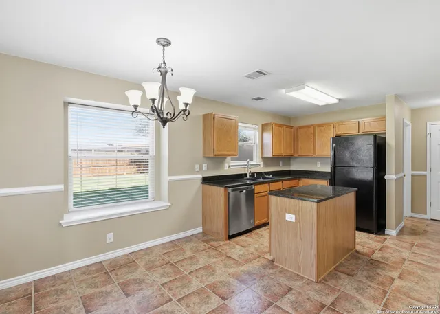 a kitchen with stainless steel appliances granite countertop a stove top oven a refrigerator a sink and a chandelier