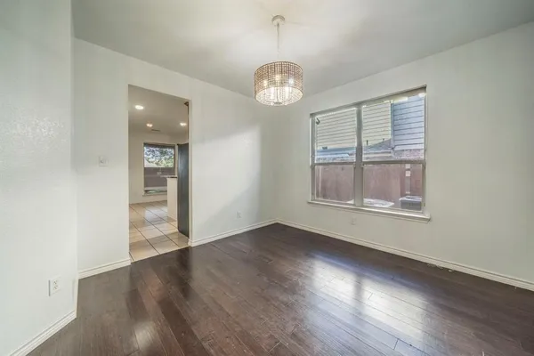 an empty room with wooden floor chandelier and windows