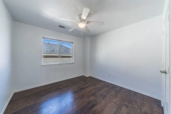 an empty room with wooden floor chandelier fan and windows