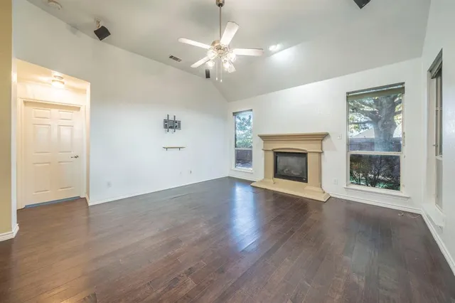 an empty room with wooden floor fireplace and windows