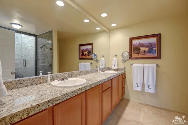 a bathroom with a granite countertop double vanity sink a mirror and a shower