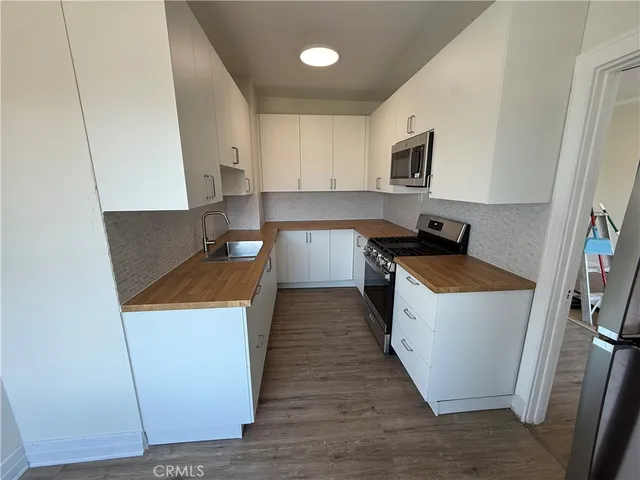 a kitchen with stainless steel appliances a stove a sink a microwave a refrigerator a sink and dishwasher with wooden floor