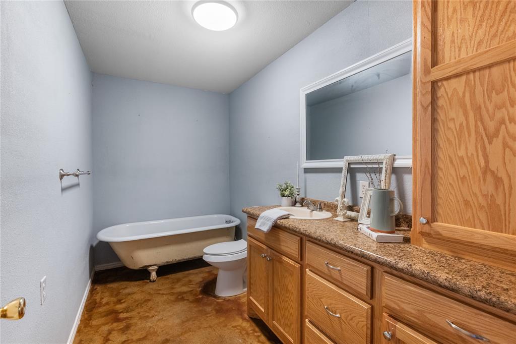 702 Main Windom, TX 75492 - Photo 9 of 30 a bathroom with a granite countertop toilet a sink and a mirror