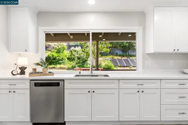 a kitchen with stainless steel appliances a stove a sink a microwave a refrigerator and white cabinets with wooden floor