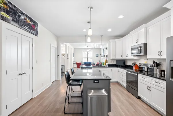 a kitchen with stainless steel appliances kitchen island granite countertop a refrigerator a sink dishwasher a stove and white cabinets with wooden floor