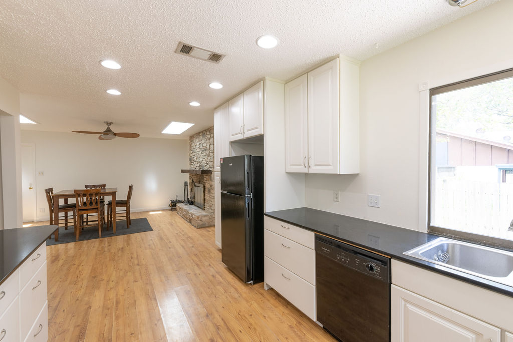 5310 Presidio Road Austin, TX 78745 - Photo 8 of 34 A well-lit kitchen with sleek black countertops and a dining area beyond, centered by a cozy stone fireplace.