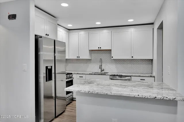 a kitchen with stainless steel appliances granite countertop a refrigerator a sink and white cabinets
