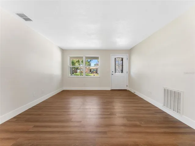 a view of an empty room with wooden floor and a window