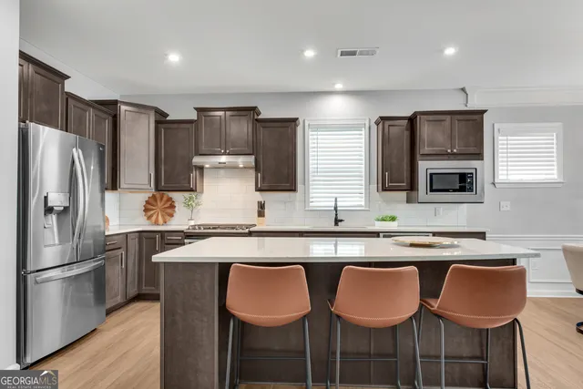 a kitchen with stainless steel appliances granite countertop a sink a stove a refrigerator and chairs