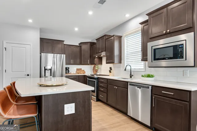 a kitchen with stainless steel appliances granite countertop a sink a stove a refrigerator cabinets and chairs