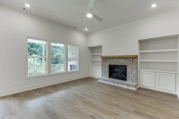 a view of an empty room with wooden floor fireplace and a window